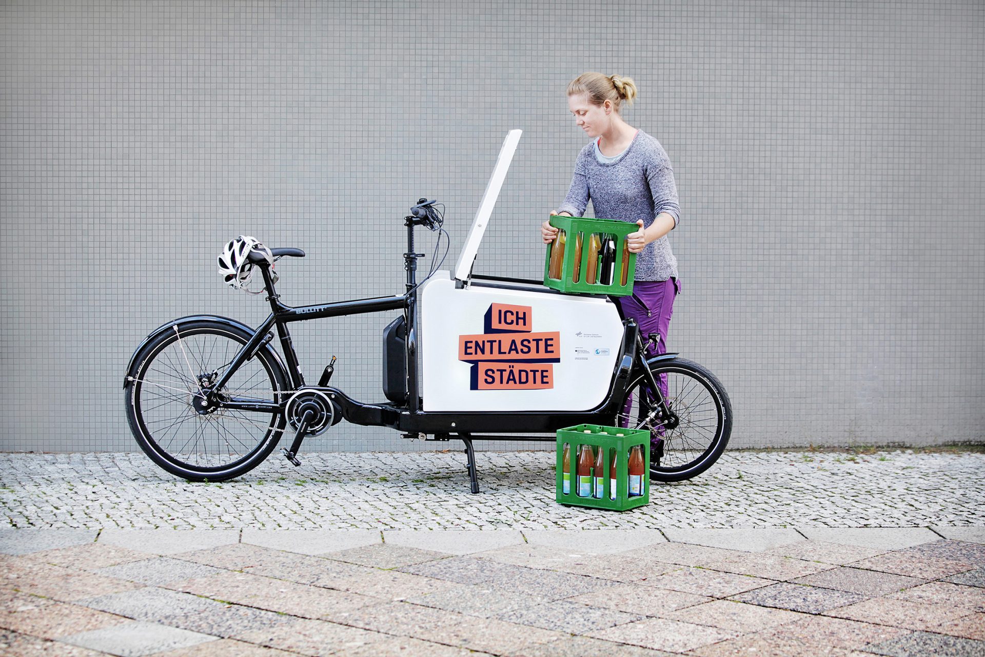 Una mujer carga una bicicleta de carga con cajas de bebidas. En la bicicleta va 